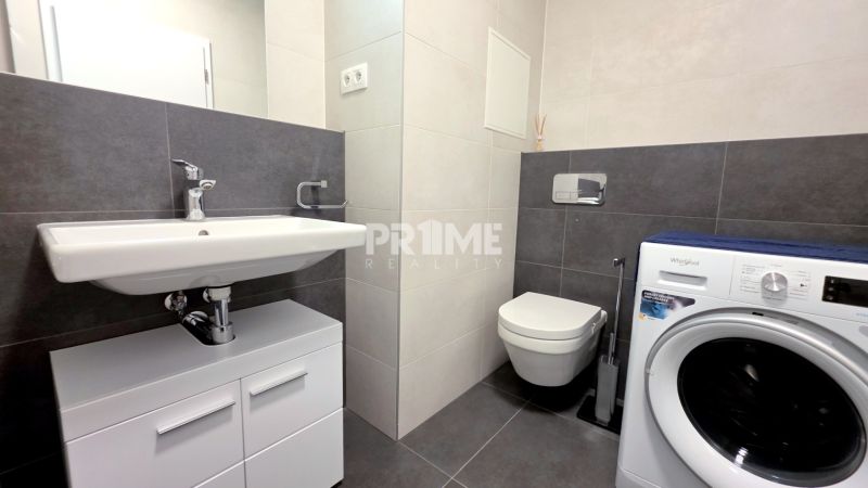 MODERNÝ 2i byt, POD VINICOU, LOGGIA, PARKING, Nové Mesto - Kúpeľňa v 2-izbovom byte s práčkou, umývadlom a tmavými obkladmi na stenách.