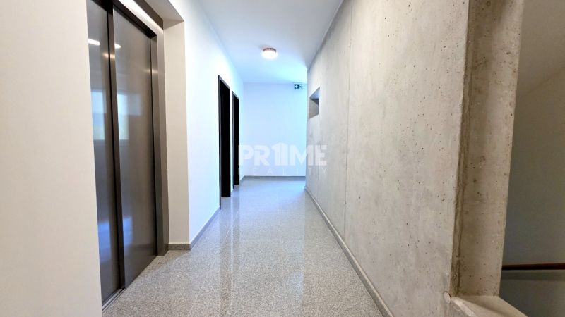 MODERNÝ 2i byt, POD VINICOU, LOGGIA, PARKING, Nové Mesto - Chodba s výťahom, schodiskom a betónovou stenou v bytovom dome.