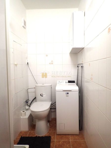 Krásny, moderne zariadený 1 izbový byt na prenájom - Kúpeľňa v 1-izbovom byte s práčkou, toaletou a bielymi dlaždicami.