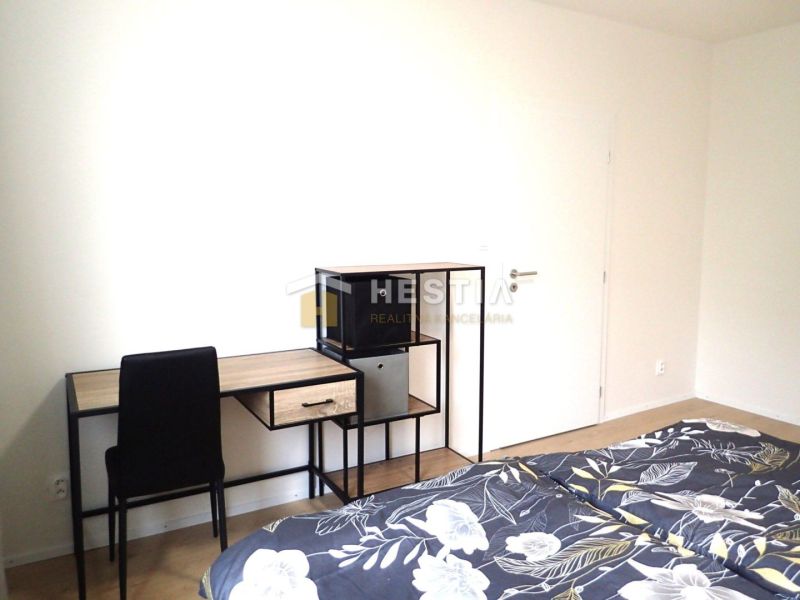 Krásny, moderne zariadený 1 izbový byt na prenájom - Izba s posteľou, pracovným stolom, čiernou stoličkou a podlahou s dreveným dekorom.