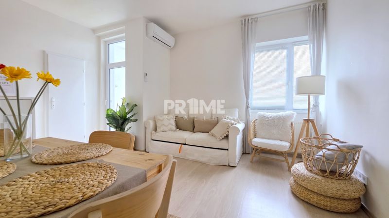 ŠTÝLOVÝ 2i BYT, REKONŠTRUKCIA, BALKÓN, KLÍMA, Murgašová ulica - Obývacia izba v 2-izbovom byte s pohovkou a košíkom na podlahe s dreveným dekorom.