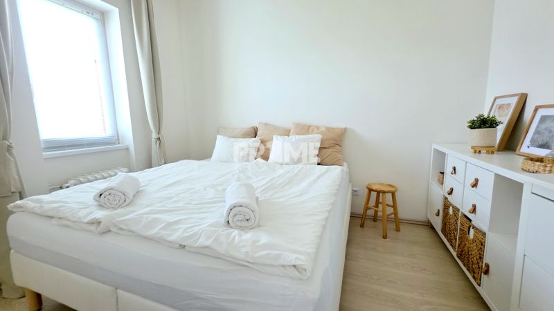 ŠTÝLOVÝ 2i BYT, REKONŠTRUKCIA, BALKÓN, KLÍMA, Murgašová ulica - Svetlá spálňa s posteľou, bielymi stenami, komodou a podlahou s dreveným dekorom.