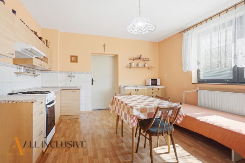 RODINNÝ DOM - CHALUPA S VEĽKÝM POZEMKOM | SKÝCOV - Kuchyňa v rodinnom dome s podlahou s dreveným dekorom, jedálenským stolom a oranžovými stenami.
