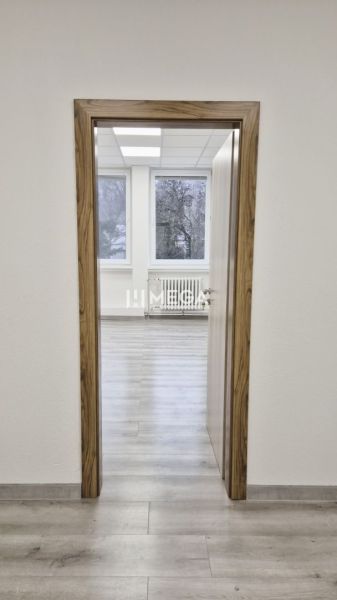 PRENÁJOM komerčného priestoru (26 m2) blízko centra Humenné - Priestor s podlahou s dreveným dekorom, biele steny a rádiator.
