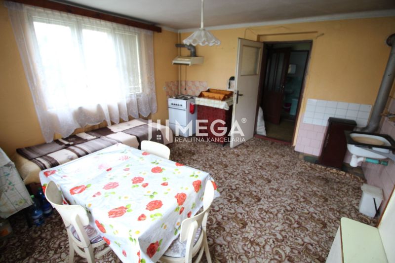 REZERVOVANÝ - Pôvodný rodinný dom v obci Dlhé nad Cirochou - Kuchyňa v Rodinnom dome s kobercom, stolom a gaučom, svetlo zo širokého okna.