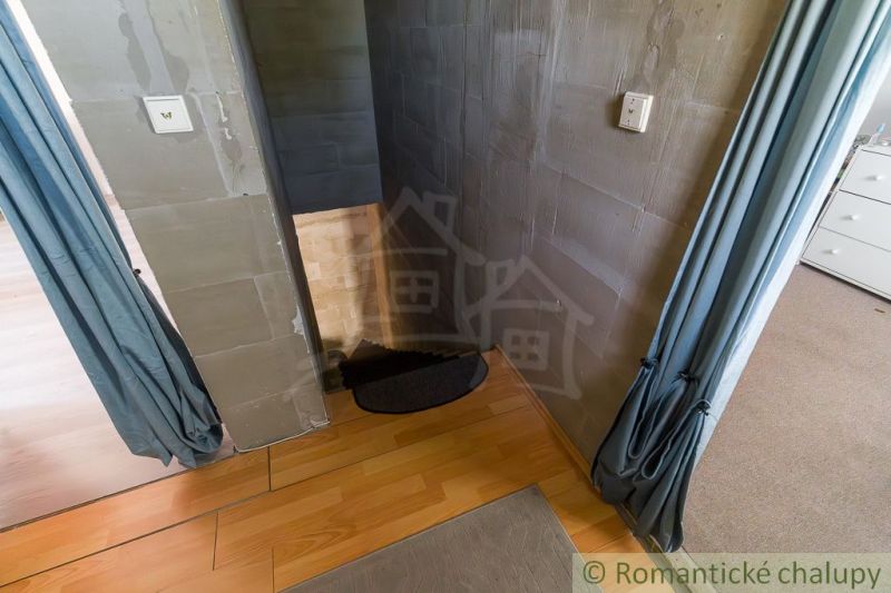 Pokojné bývanie v záhradkárskej osade s možnosťou rekreačného aj celor - Interiér chaty so schodmi a podlahou s dreveným dekorom, doplnený závesmi.