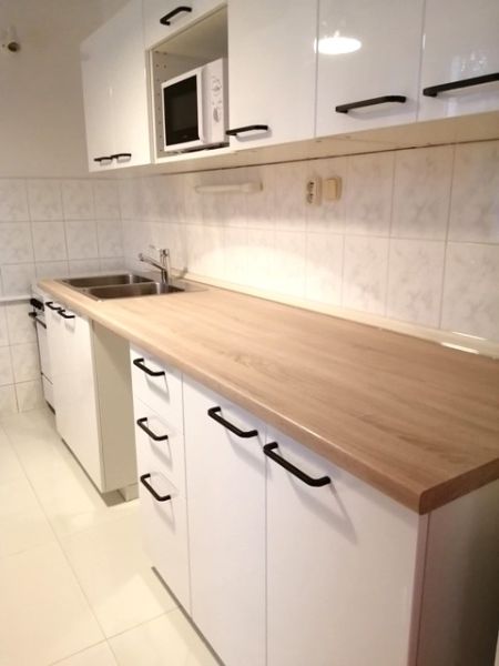 PRENÁJOM: ÚTULNÝ 2 IZBOVÝ BYT S BALKÓNOM, UHLISKO - Kuchyňa v 2-izbovom byte s bielymi skrinkami a podlahou s dreveným dekorom.