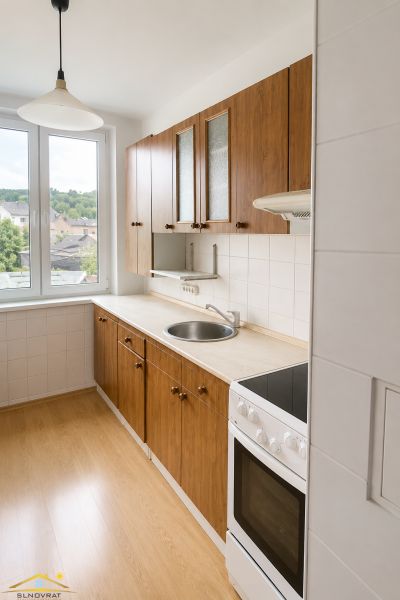 Na predaj: 3-izbový byt v meste Krásno nad Kysucou - Kuchyňa 3-izbového bytu s dverami na balkón a podlahou s dreveným dekorom.