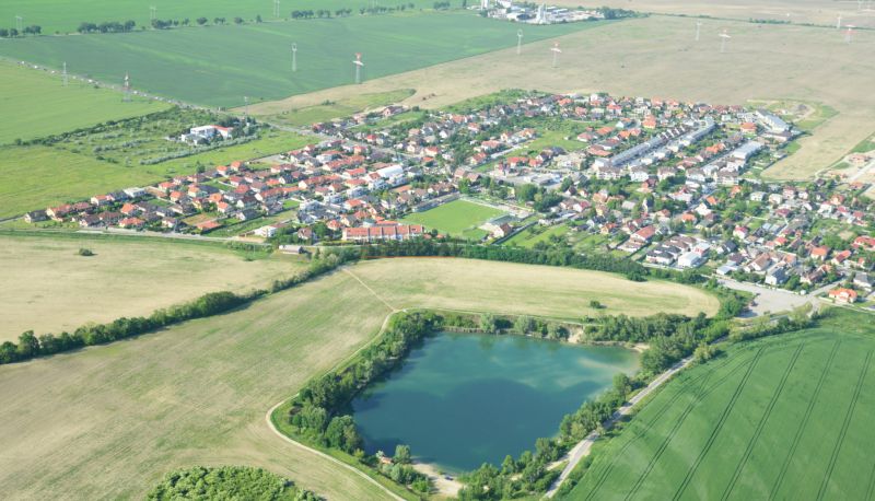 3-izb. byt na prenájom, Rovinka – novostavba, klimatizácia, parkovanie - Letecký pohľad na Rovinku a okolitú krajinu s jazerom a domami.