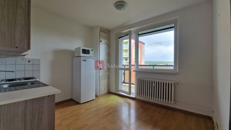 AstonReal: predaj 2-izbovy byt 57m2 + loggia, Kežmarok - K. Kuzmányho - Kuchyňa v 2-izbovom byte s podlahou s dreveným dekorom, chladničkou a výhľadom z balkóna.