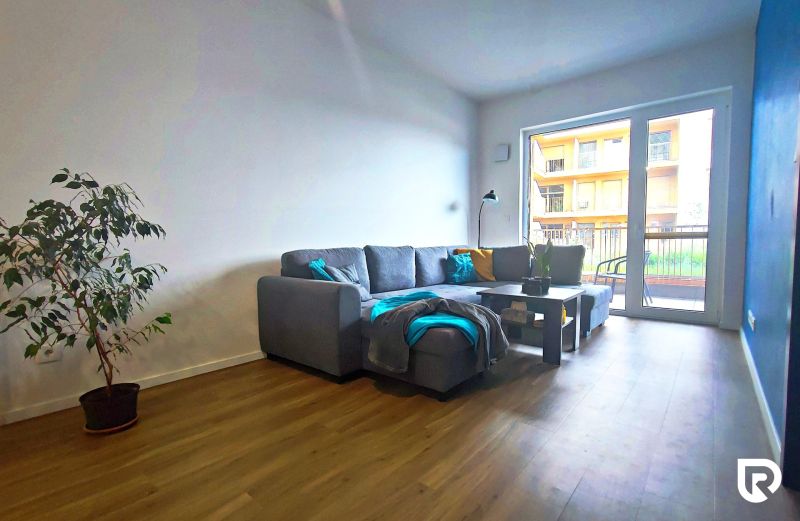 | Srdce Mesta | 2 Izb. byt | ORBIS |  70 m2 - Obývacia izba v 2-izbovom byte s pohovkou, rastlinou a podlahou s dreveným dekorom.