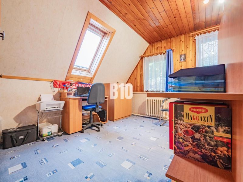 Bývanie alebo podnikanie priamo pod HRADOM? - Izba s dreveným stropom, oknom, písacím stolom a modrým kobercom v rodinnom dome.