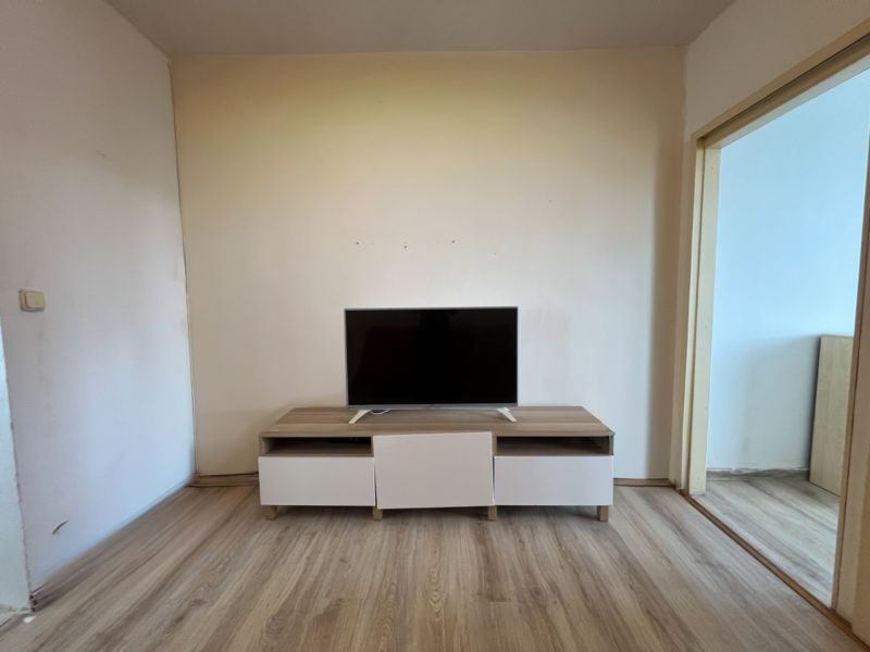 Na predaj 1-izbový byt s loggiou - Žiar nad Hronom, M. Chrasteka 1B718 - Izba s TV na skrinke, podlaha s dreveným dekorom, priestor v 1-izbovom byte.