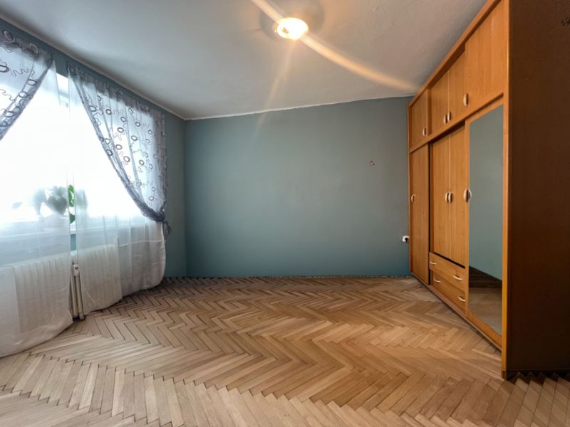 Na predaj 3-izbový byt s loggiou – Žiar nad Hronom, ul. D. Hrdinov - Izba s podlahou s dreveným dekorom, šatníkovou skriňou a záclonami v 2-izbovom byte.