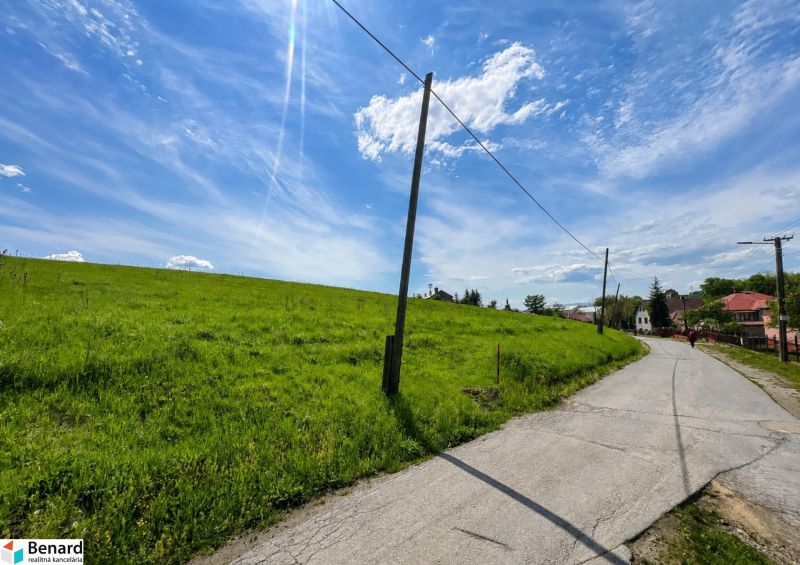 Priestranný stavebný pozemok 2 441 m² vo Finticiach - Cesta vedúca popri zelených pozemkoch na bývanie vo Finticiach pod modrou oblohou.