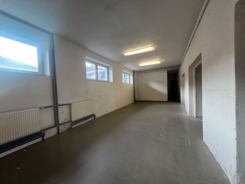 Sklad + kancelárie 1349 m² logistický objekt s rampami -Banská Bystria - Dlhá miestnosť s bielymi stenami, oknami a liatinovými radiátormi v skladoch a halách.
