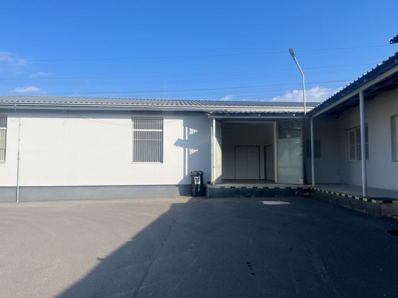 Skladové a výrobné priestori s kanceláriami 130 m² /180 m² /198 m² BB - V areáli skladov a hál v okrese Banská Bystrica, pred bielou budovou s dverami.