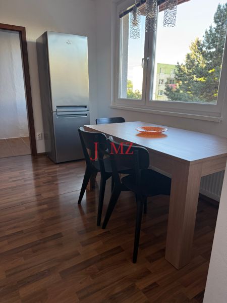 Prenájom 3-izb. byt Ku Bratke - zariadený - Jedálenský kút s tromi stoličkami a stolom, vedľa chladničky, podlaha s dreveným dekorom.