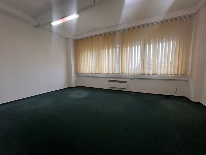 Na prenájom kancelária 24m2 - Banská Bystrica, Zvolenská cesta NO556ZL - Prázdna kancelária s tmavým kobercom a veľkými oknami so žalúziami.