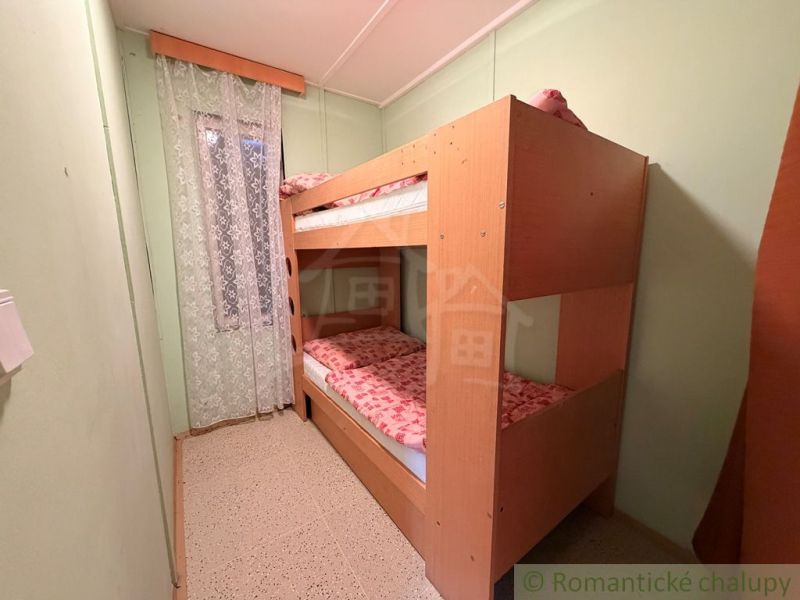 AREÁL 3 REKREAČNÝCH CHÁT PRI PODHÁJSKEJ – IDEÁLNE PRE DETSKÉ TÁBORY, R - Poschodová posteľ v izbe chaty so závesom s kvetinovým vzorom.