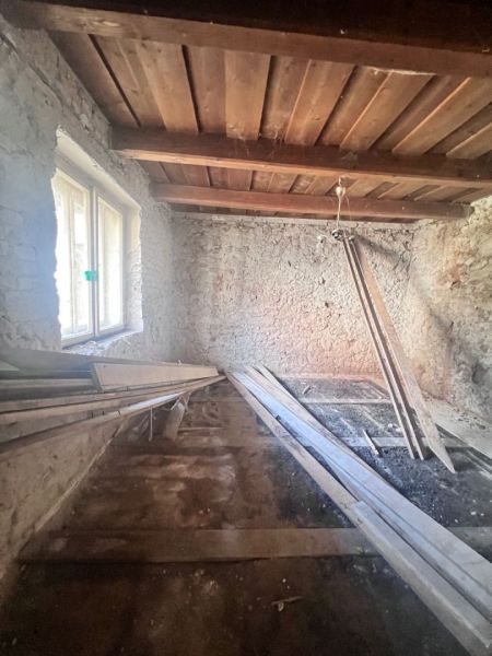 Na predaj vidiecky rodinný dom - Žarnovica/Brehy D045ZL - Izba v rodinnom dome s kamennými stenami a dreveným stropom, materiál na podlahe.