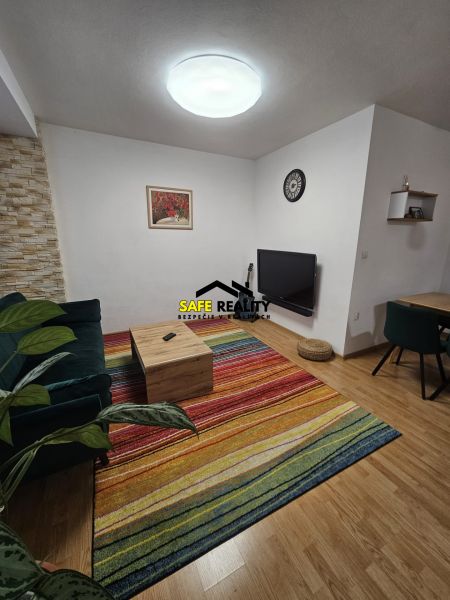 3 - izbový byt Žilina - Závodie, Exkluzívne - Obývacia izba v 3-izbovom byte s farebným kobercom a podlahou s dreveným dekorom.