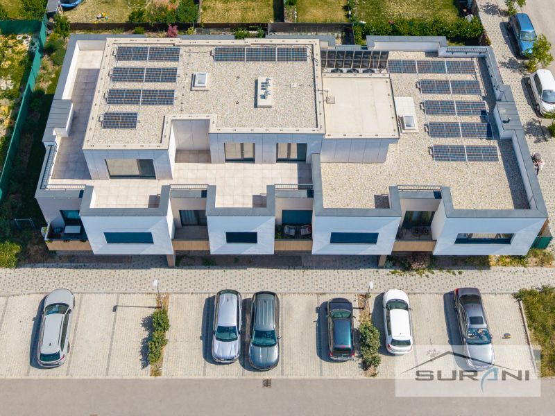 Nový 3-izbový byt 82 m² | Terasa 97 m² | Mesačná ulica | Hviezdoslavov - Budova na Mesačnej ulici v Hviezdoslavove so solárnymi panelmi a zaparkovanými autami.