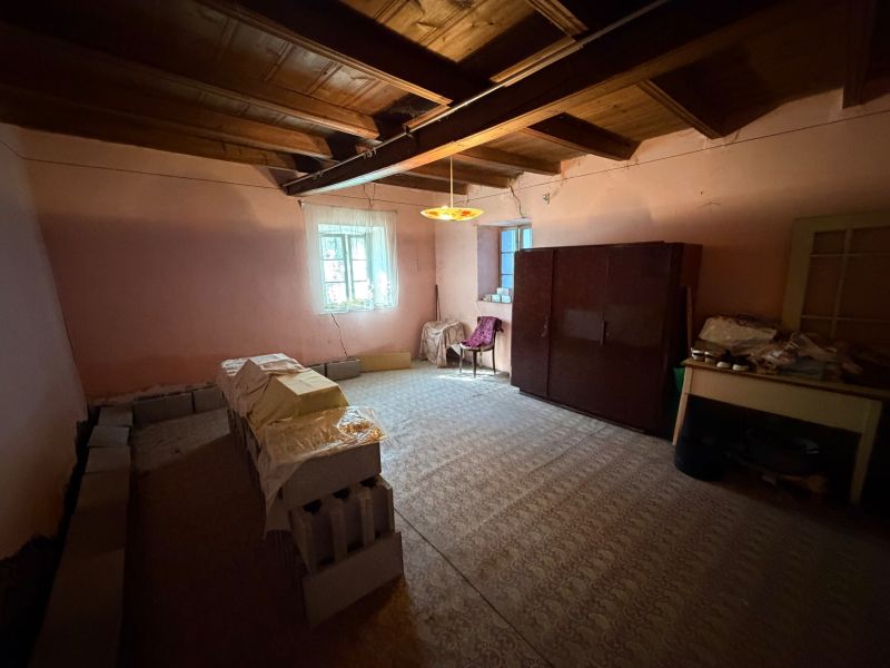 Rodinný dom s veľkým pozemkom v meste Nesvady  - Izba v rodinnom dome s nábytkom, stohmi tehál a dreveným stropom.