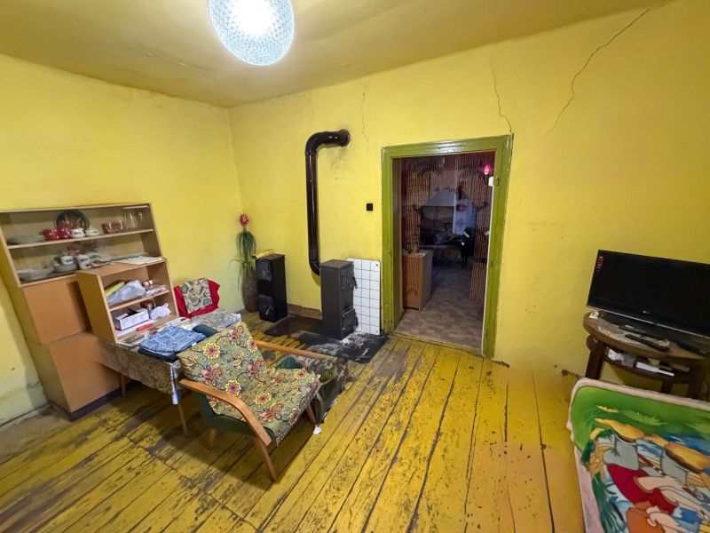 Rodinný dom s veľkým pozemkom v meste Nesvady  - Obývačka v rodinnom dome s pecou, žltými stenami a podlahou s dreveným dekorom.