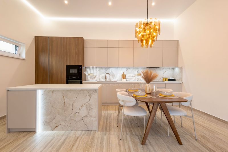 MODERNÝ 4-IZBOVÝ BUNGALOV | ZEMPLÍNSKA ŠIROKÁ - Kuchyňa s ostrovčekom, podlaha s dreveným dekorom, jedálenský stôl a zlatý luster.