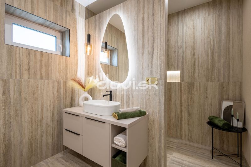 MODERNÝ 4-IZBOVÝ BUNGALOV | ZEMPLÍNSKA ŠIROKÁ - Kúpeľňa s oválnym zrkadlom a prírodnými tónmi, podlaha s dreveným dekorom.