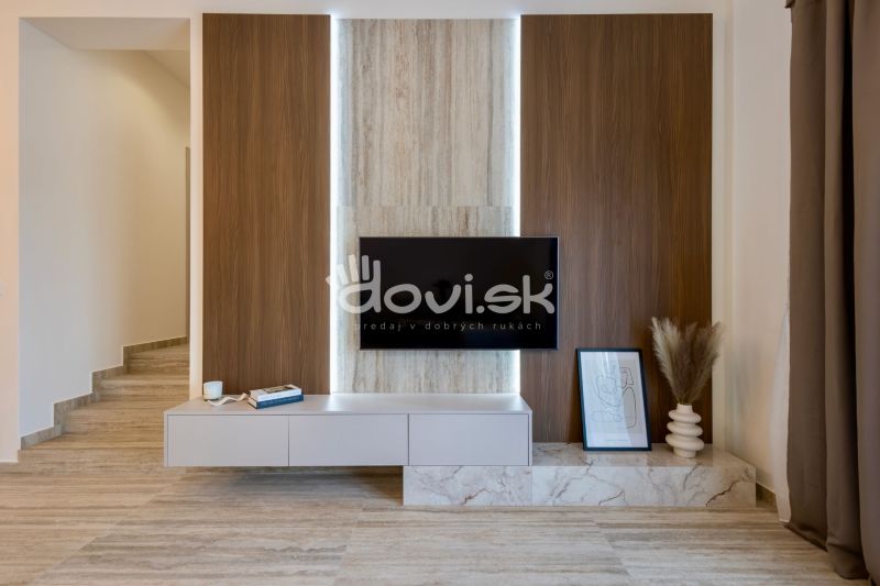 MODERNÝ 4-IZBOVÝ BUNGALOV | ZEMPLÍNSKA ŠIROKÁ - Interiér rodinného domu so stenou s dreveným dekorom, televízorom a dekoráciami.