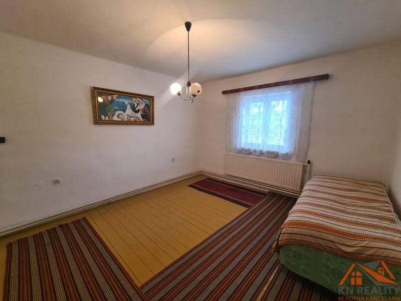 Na predaj rodinný dom Dulovce ! - Interiér rodinného domu s posteľou, obrazom a oknom so záclonami.