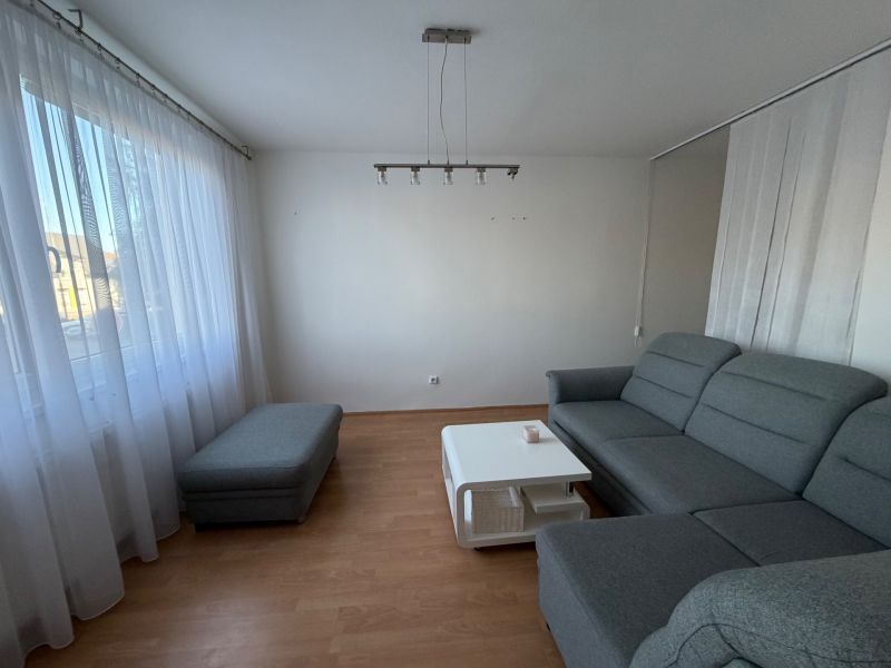 3 izbový byt s balkónom v meste Levice - Obývacia izba so sivou sedačkou, stolíkom a podlahou s dreveným dekorom v 3-izbovom byte.