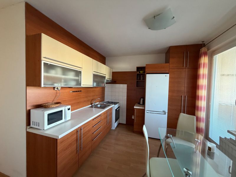 3 izbový byt s balkónom v meste Levice - Kuchyňa v 3-izbovom byte s bielou linkou a podlahou s dreveným dekorom.