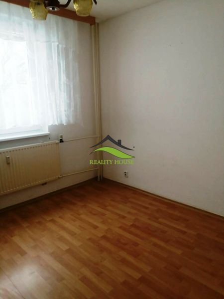 3 izbový byt na sidlisku Stráňany - Miestnosť v 3-izbovom byte s podlahou s dreveným dekorom, závesom a radiátorom.