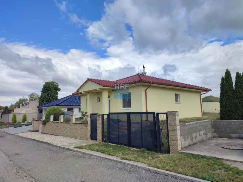 Na predaj zariadený 3izbový bungalov v obci Radimov - Rodinný dom v Radimove s červenou strechou, udržiavanou záhradou a betónovým plotom.