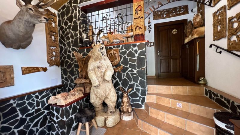 Na predaj penzion  – Štôla, Vysoké Tatry O560ZL - Interiér vily s drevenými sochami zvierat a kamennými stenami.