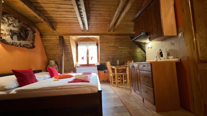 Na predaj penzion  – Štôla, Vysoké Tatry O560ZL - Drevené trámy, posteľ, kuchynský kút a stôl v podkroví vo Vile.