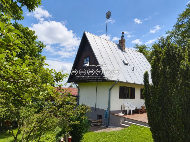 Exkluzívne na predaj, čarovný rodinný dom / chalupa v lone prírody - Rodinný dom na ulici Horné Otrokovce v Horných Otrokovciach obklopený zeleňou a modrou oblohou.