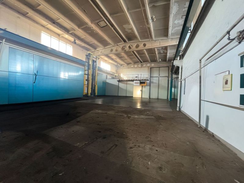 Na prenájom priestor 378 m² s vykurovaním — Banská Bystrica, Majer  - Výrobné priestory s vysokým stropom, ktoré majú bledomodré dvere a trubky na stenách.