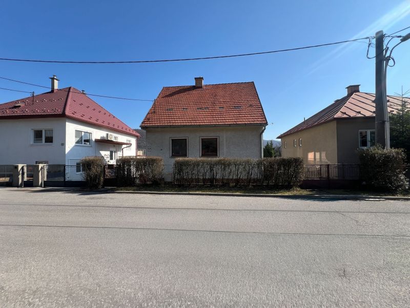 ROVINATÝ POZEMOK  S PRÍSTUPOM Z DVOCH STRÁN+ RODINNÝ DOM – B. Bystrica - Rodinný dom v Banskej Bystrici s červenou strechou a kríkovým plotom.