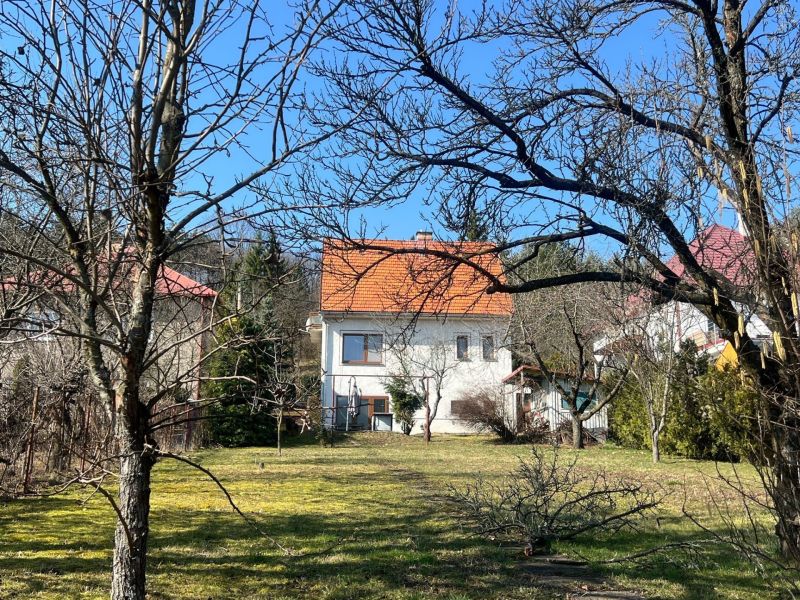 ROVINATÝ POZEMOK  S PRÍSTUPOM Z DVOCH STRÁN+ RODINNÝ DOM – B. Bystrica - Rodinný dom v Podháji, Kráľovej, obklopený stromami a trávnikom, s oranžovou strechou.