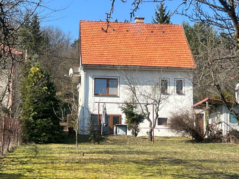 ROVINATÝ POZEMOK  S PRÍSTUPOM Z DVOCH STRÁN+ RODINNÝ DOM – B. Bystrica - Rodinný dom v Kráľovej, Banská Bystrica, s červenou strechou obklopený zeleňou a stromami.