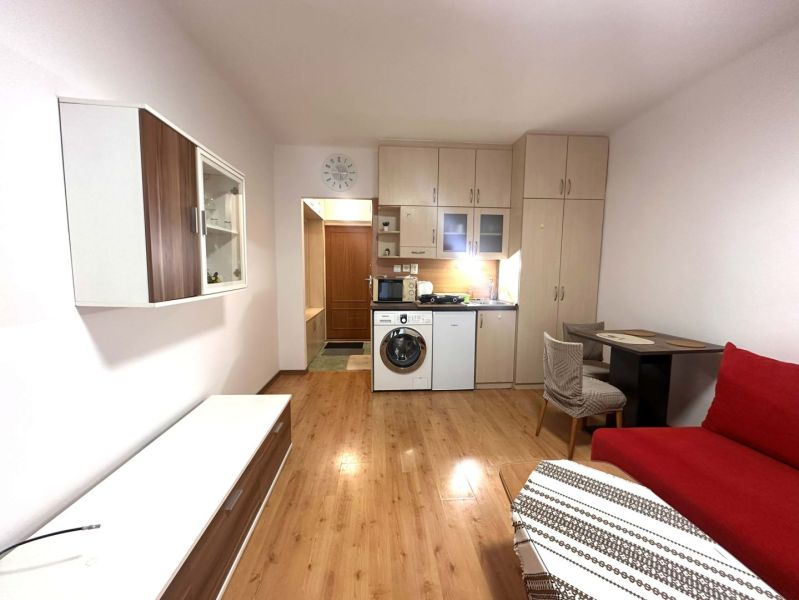 ☎️ 0918/197 701 Na prenájom garsónka s balkónom aj s výťahom   v centr - Rekreačný apartmán so vstavanou kuchyňou, červenou sedačkou a podlahou s dreveným dekorom.