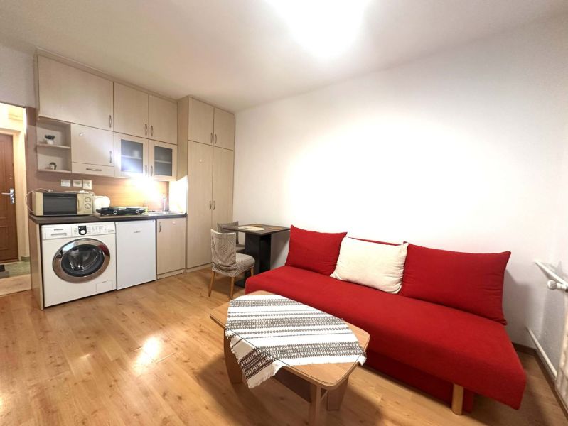 ☎️ 0918/197 701 Na prenájom garsónka s balkónom aj s výťahom   v centr - Rekreačný apartmán s červenou sedačkou, kuchynským kútom a podlahou s dreveným dekorom.