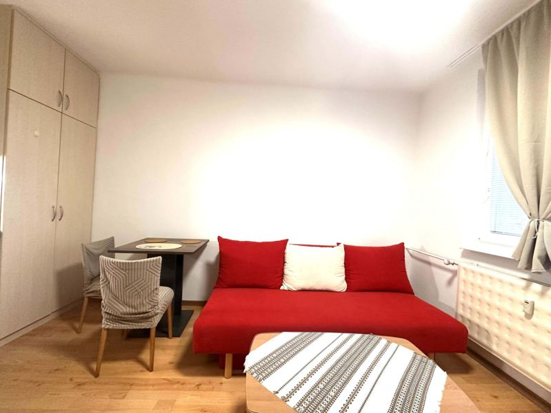 ☎️ 0918/197 701 Na prenájom garsónka s balkónom aj s výťahom   v centr - Izba v rekreačnom apartmáne s červenou pohovkou, stolom, a podlahou s dreveným dekorom.