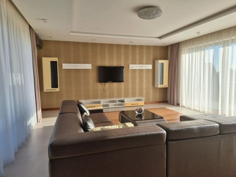 PRENÁJOM- Jedinečný, luxusný byt 148 m2 s terasami a parkovaním -Nitra - Obývacia izba s hnedou sedačkou, televízorom na stene a veľkými oknami. Idealne pre 4-izbový byt na ulici Dolnohorská.