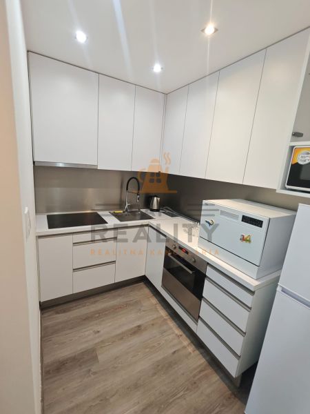Na prenájom 1 izbový byt, 34 m2, Bratislava, Petržalka, Lachova ulica - Kuchynská linka v 1-izbovom byte so spotrebičmi a podlahou s dreveným dekorom.