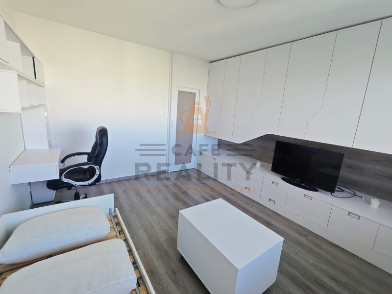 Na prenájom 1 izbový byt, 34 m2, Bratislava, Petržalka, Lachova ulica - Interiér 1-izbového bytu s pracovným stolom, televízorom a podlahou s dreveným dekorom.